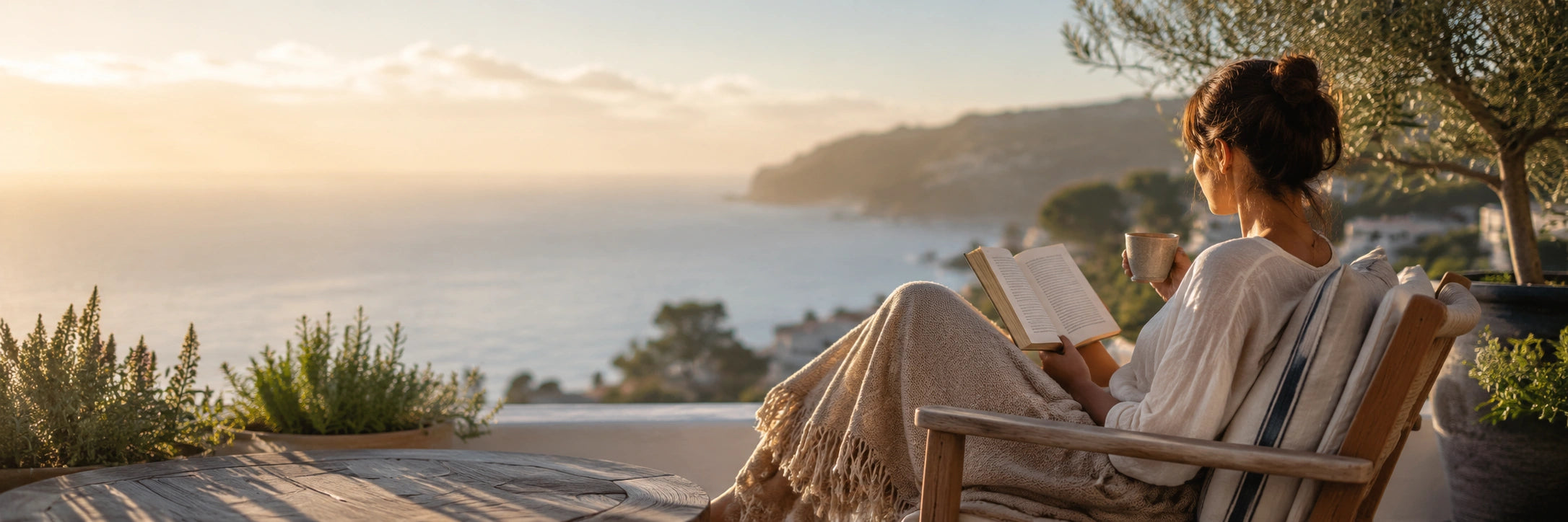 Woman reading a book on a bench by the ocean at sunset