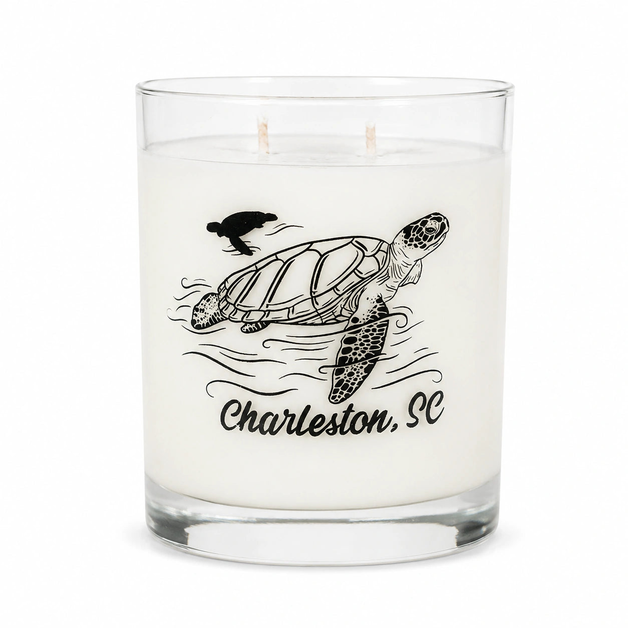 A white scented candle in a clear glass jar with two wicks, featuring a black line art illustration of a sea turtle, waves, a bird, and the text 'Charleston, SC' on the front.