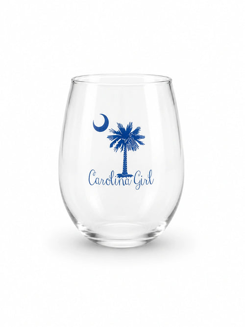 A clear stemless wine glass with a blue printed design featuring a crescent moon, a palm tree, and the words 'Carolina Girl' on a white background.