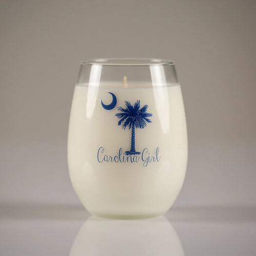 White candle in a glass container with blue 'Carolina Girl' design on a neutral background