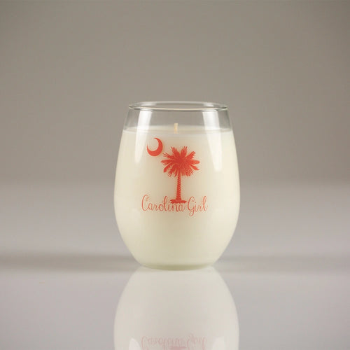 Glass candle with 'Carolina Girl' and palm tree design on a reflective surface.