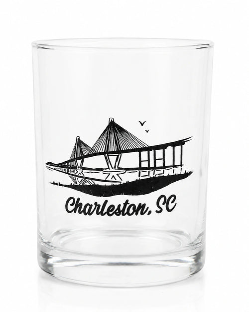 A clear glass rocks tumbler featuring a black line art graphic of the Charleston, SC bridge with the text 'Charleston, SC' printed below, shown on a white background.
