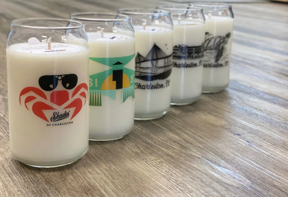 Five candles in glass containers with various designs on a wooden surface
