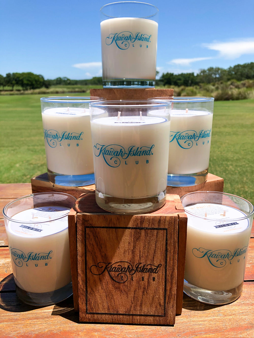 Set of candles in glass holders on a wooden stand with 'Kauai Island Club' branding, outdoors.