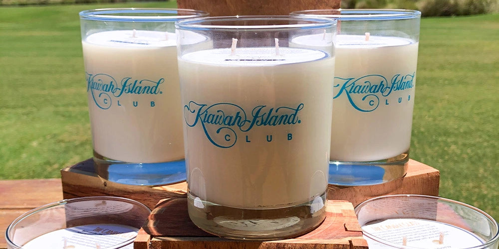 Three candles with 'Kiawah Island Club' branding on a wooden surface outdoors.