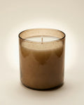 Brown glass candle with a lit wick on a beige background