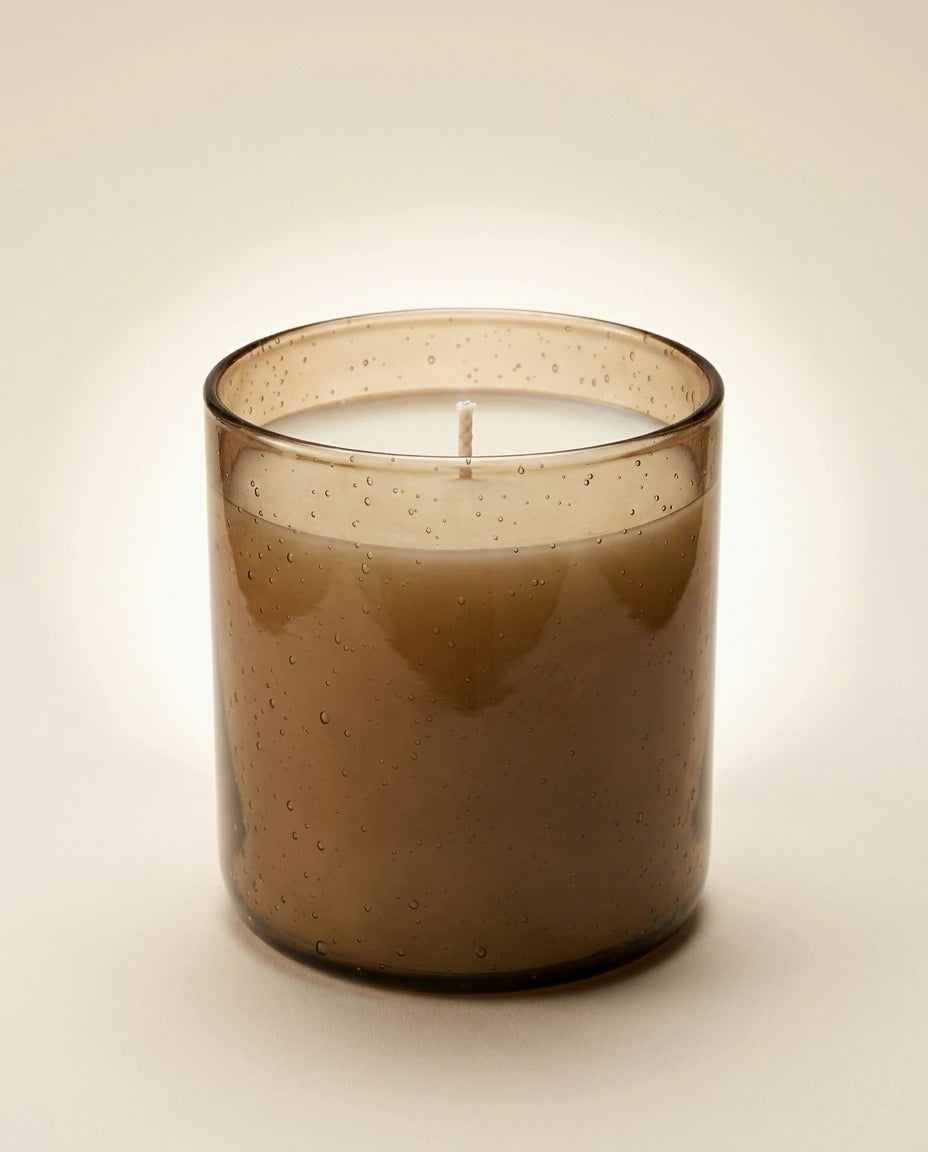Brown glass candle with a lit wick on a beige background