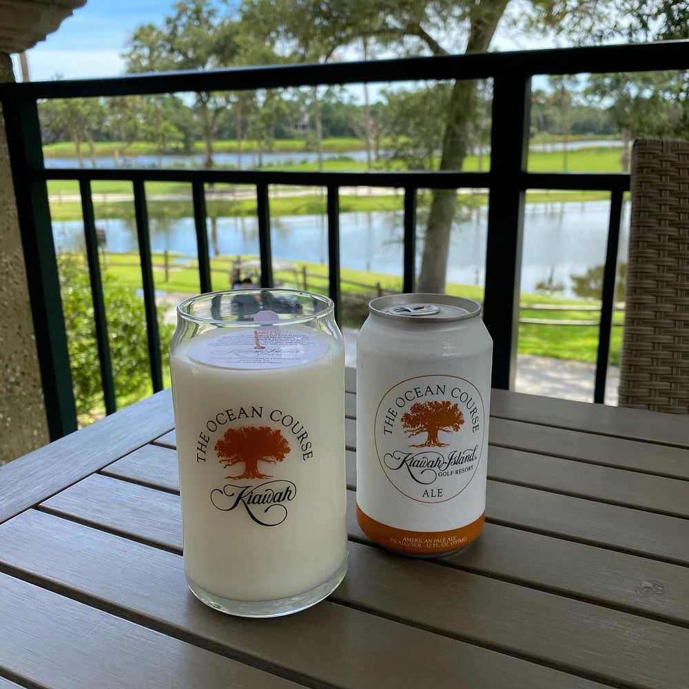 Two cans of 'The Ocean Course' beer on a table with a scenic background.